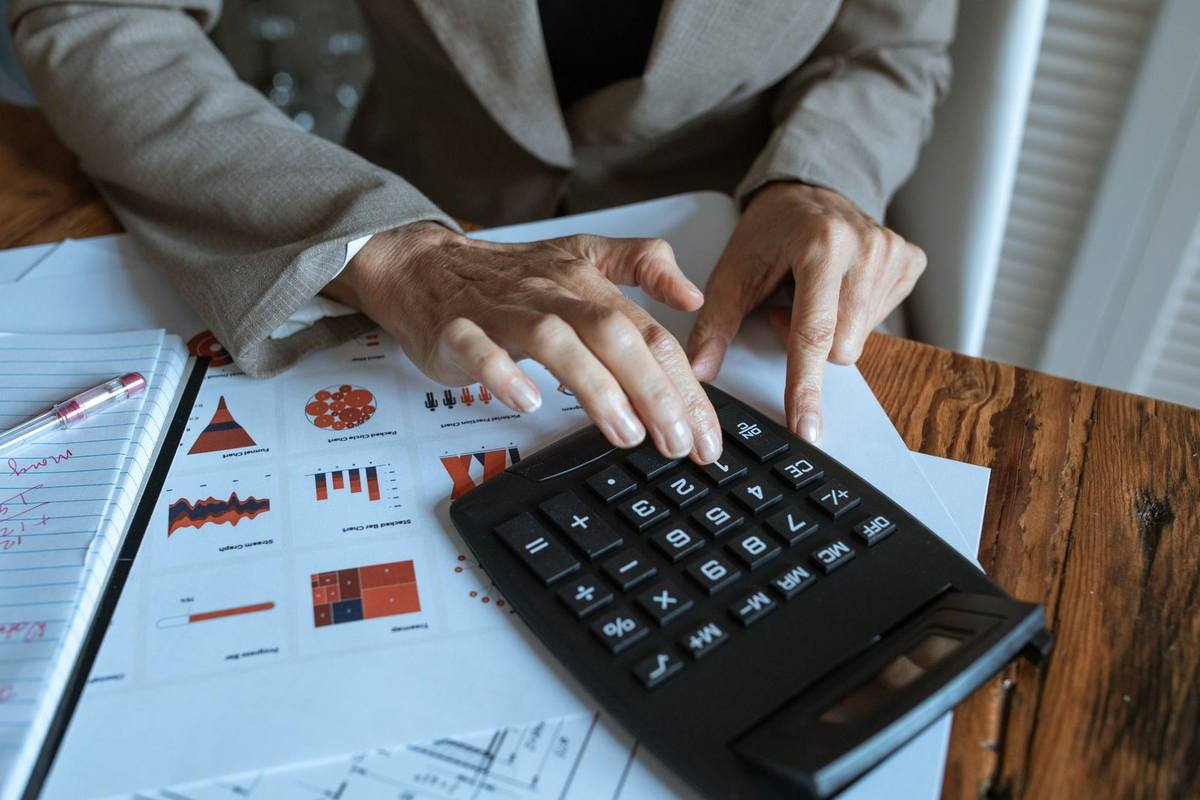 Une personne utilise un calculateur sur une table avec des documents et un stylo Une personne utilise un calculateur sur une table avec des documents et un stylo