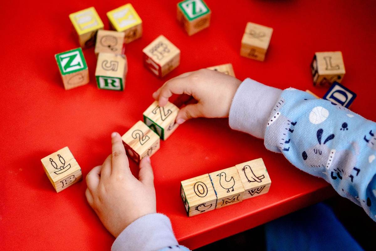 Enfant manipulant des blocs en bois avec lettres et chiffres sur une table rouge Enfant manipulant des blocs en bois avec lettres et chiffres sur une table rouge