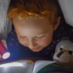 Enfant lit un livre avec une lampe torche dans son lit