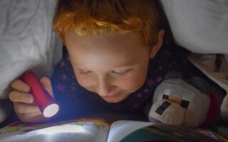 Enfant lit un livre avec une lampe torche dans son lit