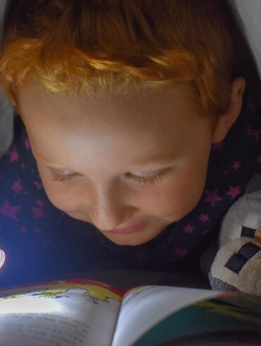 Enfant lit un livre avec une lampe torche dans son lit