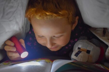 Enfant lit un livre avec une lampe torche dans son lit