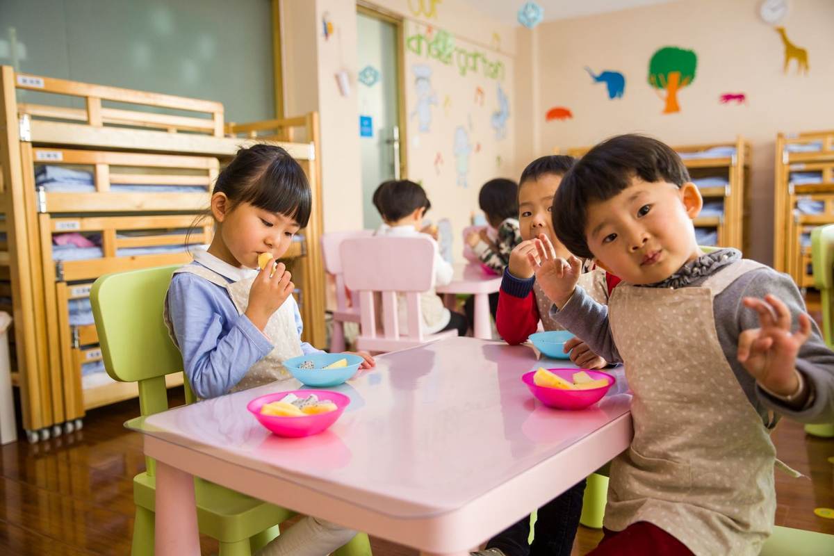 Enfants assis autour d'une table, mangeant, dans une salle de classe Enfants assis autour d'une table, mangeant, dans une salle de classe