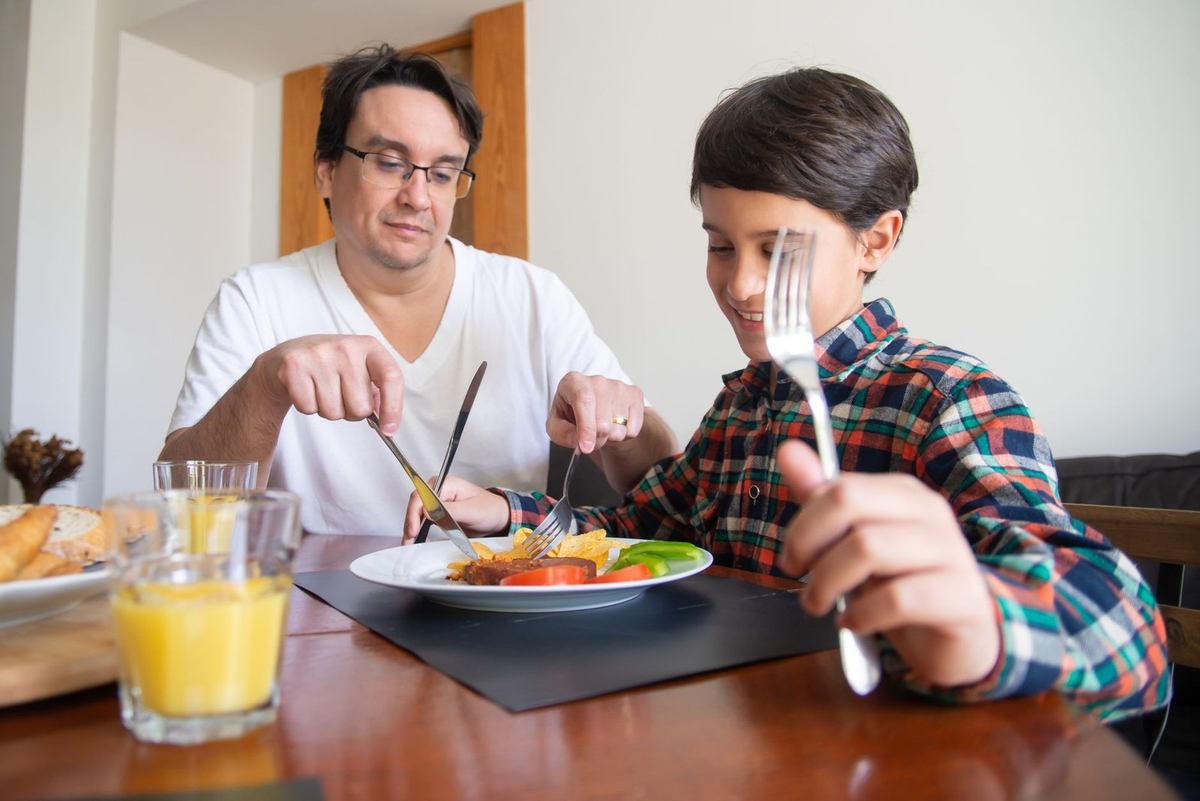 Homme et garçon partagent un repas, verres d'orangeade sur la table Homme et garçon partagent un repas, verres d'orangeade sur la table