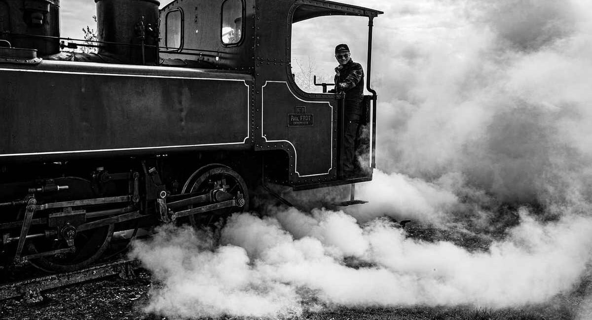 Un train à vapeur noir, conducteur visible, fumée abondante