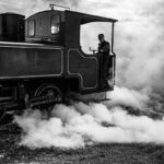 Un train à vapeur noir, conducteur visible, fumée abondante