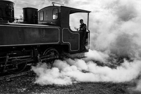 Un train à vapeur noir, conducteur visible, fumée abondante