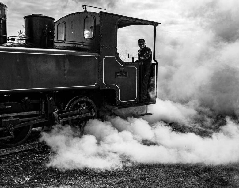 Un train à vapeur noir, conducteur visible, fumée abondante