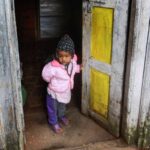 Petit enfant habillé chaudement, debout dans l'encadrement d'une porte