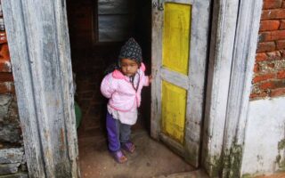 Petit enfant habillé chaudement, debout dans l'encadrement d'une porte