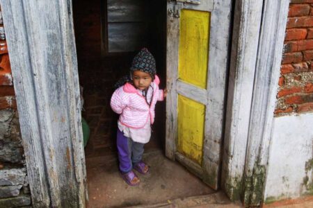 Petit enfant habillé chaudement, debout dans l'encadrement d'une porte