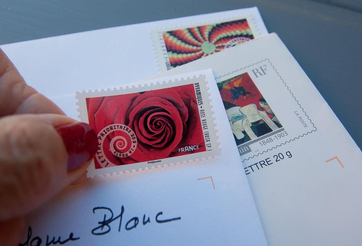 Une main tenant une enveloppe avec timbres colorés Une main tenant une enveloppe avec timbres colorés